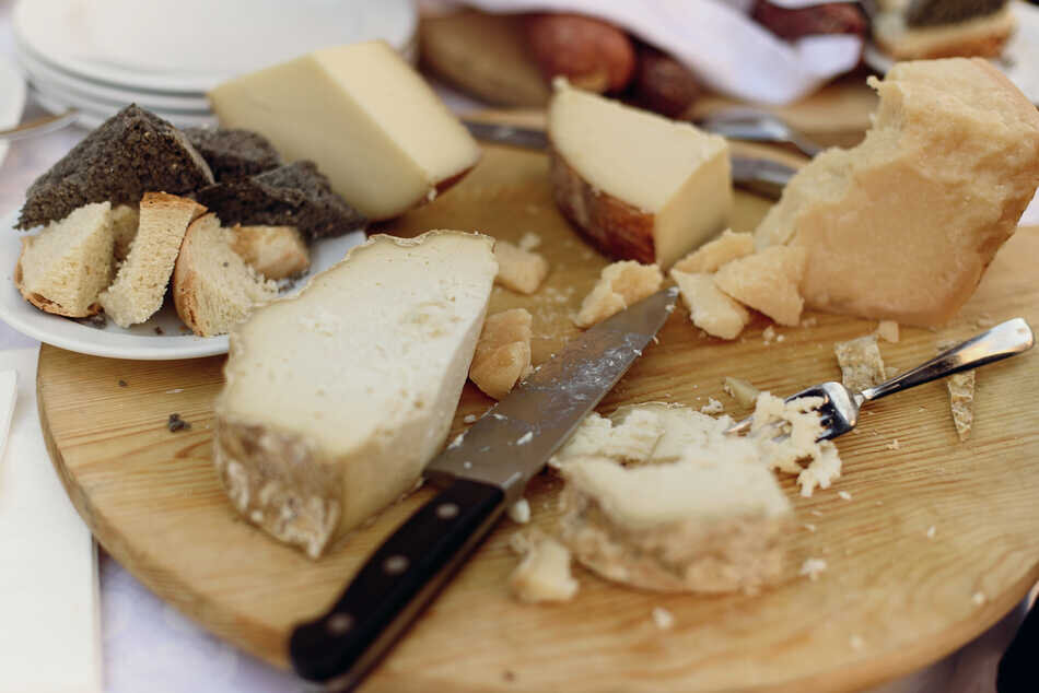 Knife and fork lie on wooden plate with different kinds of cheese